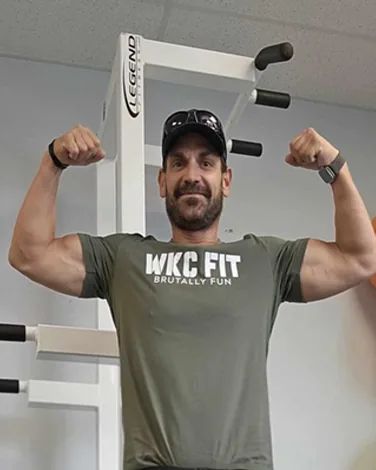 Jason Derganc flexing both arms in front of a white exercise station