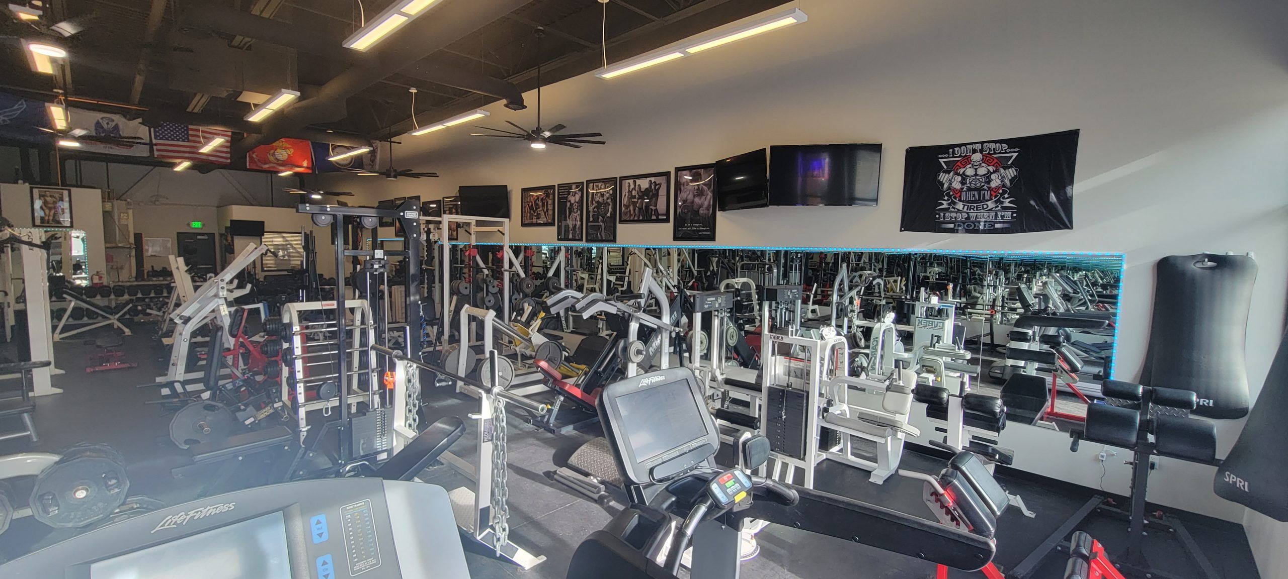 Main training floor with selectorized machines, plate-loaded stations and a mirrored wall under American and Marine Corps flags